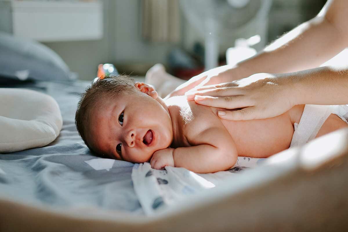 baby on stomach with parent's hands on back