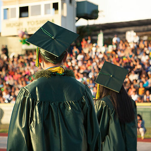 Two graduates facing the crowd